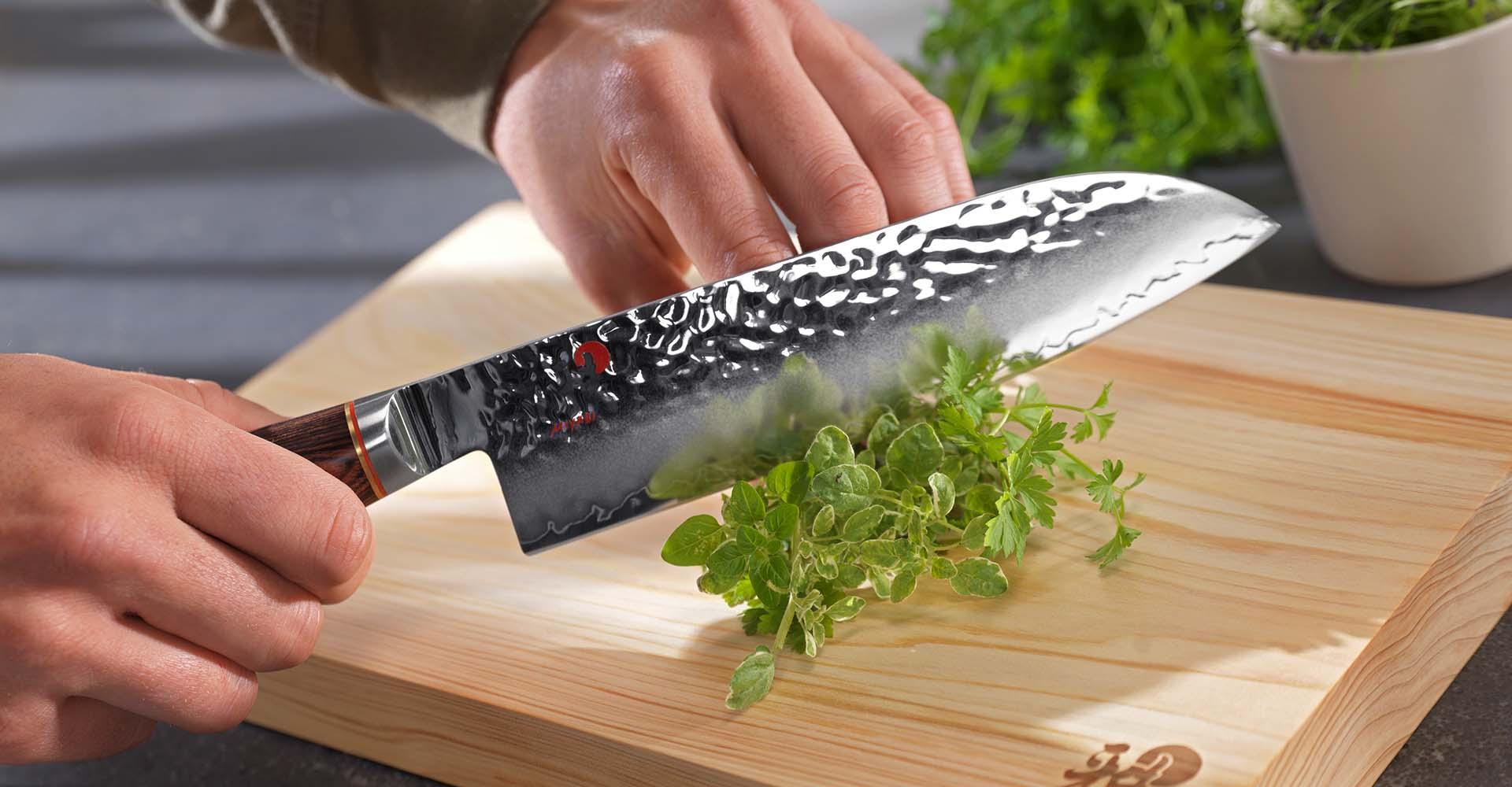 Japoński nóż Santoku do krojenia ziół na desce. Nóż Santoku krojący zioła na drewnianej desce w kuchni.