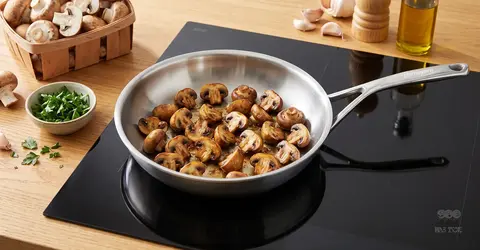 Rumiane pieczarki smażone na stalowej patelni na płycie indukcyjnej, świeże zioła i składniki obok