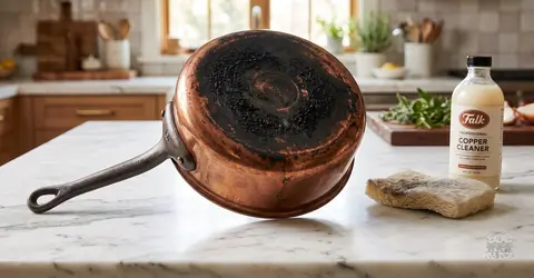 Miedziany rondel z przypalonym dnem, środek do czyszczenia miedzi i gąbka na marmurowym blacie kuchennym