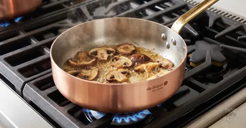 Smażone pieczarki w miedzianej patelni na kuchence gazowej, idealne do aromatycznych dań