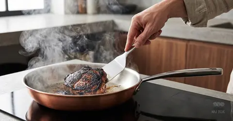 Smażenie mięsa na miedzianej patelni z widocznymi przypaleniami, ręka trzyma łopatkę kuchenną