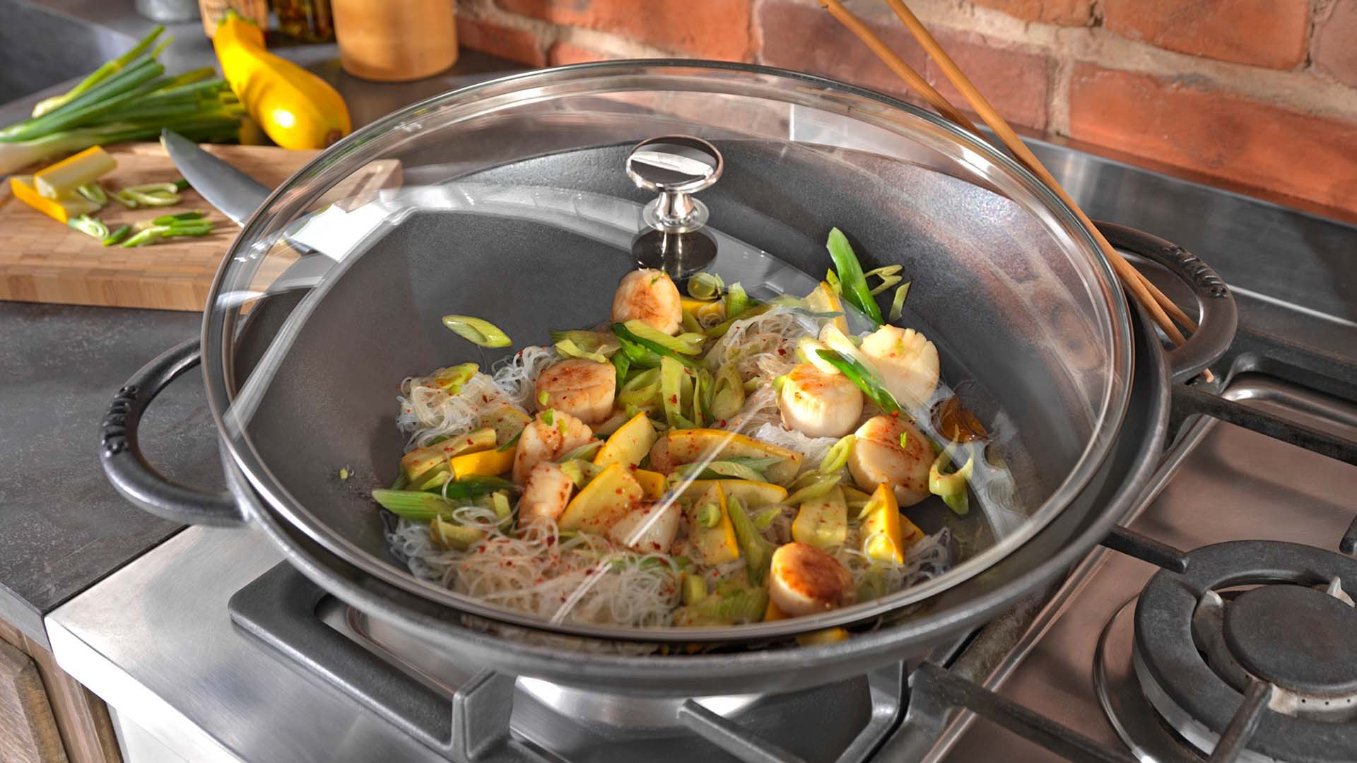 Wok żeliwny z pokrywą Staub, gotowanie makaronu z warzywami Żeliwny wok Staub z pokrywką, przygotowanie azjatyckiego dania na kuchence