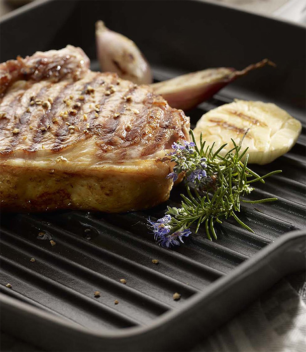 Kawałek mięsa na żeliwnej patelni grillowej z dodatkiem ziół Żeliwna patelnia grillowa z kawałkiem mięsa, czosnkiem i rozmarynem