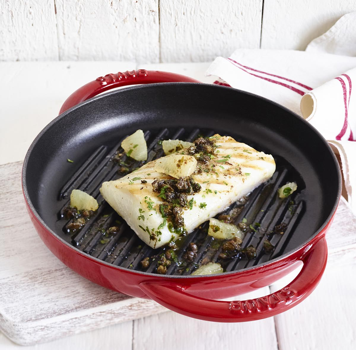 Czerwona żeliwna patelnia Staub z grillowaną rybą, porcelanowa powłoka, kolekcja Pure Grill. Żeliwna patelnia grillowa Staub z rybą i dodatkami, kolekcja Pure Grill, czerwona porcelanowa glazura.