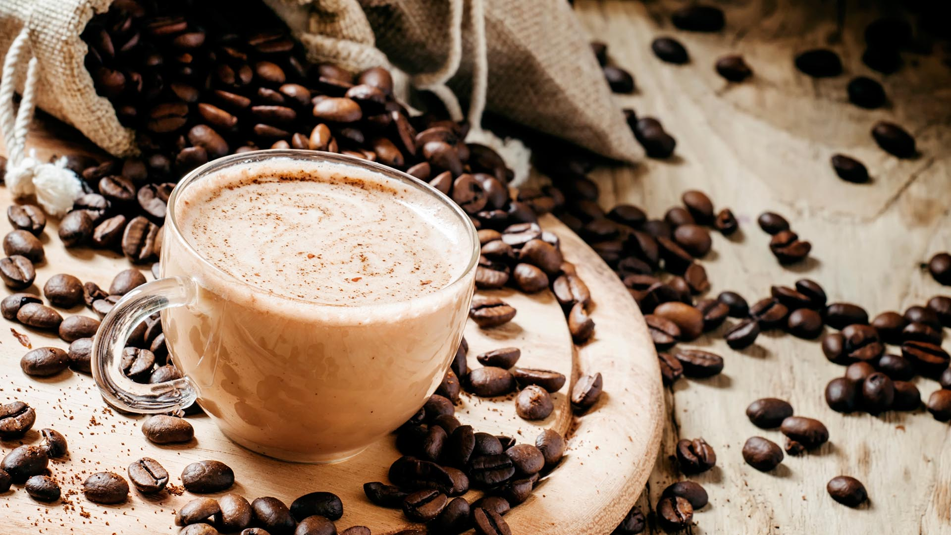 Filiżanka cappuccino otoczona ziarnami kawy na drewnianym tle.