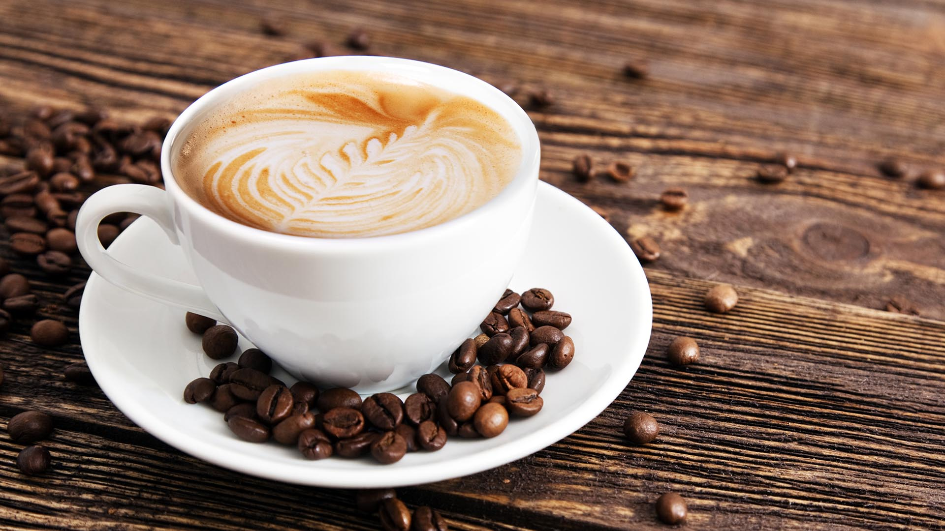 Filiżanka kawy z latte art na drewnianym stole, otoczona ziarnami kawy.