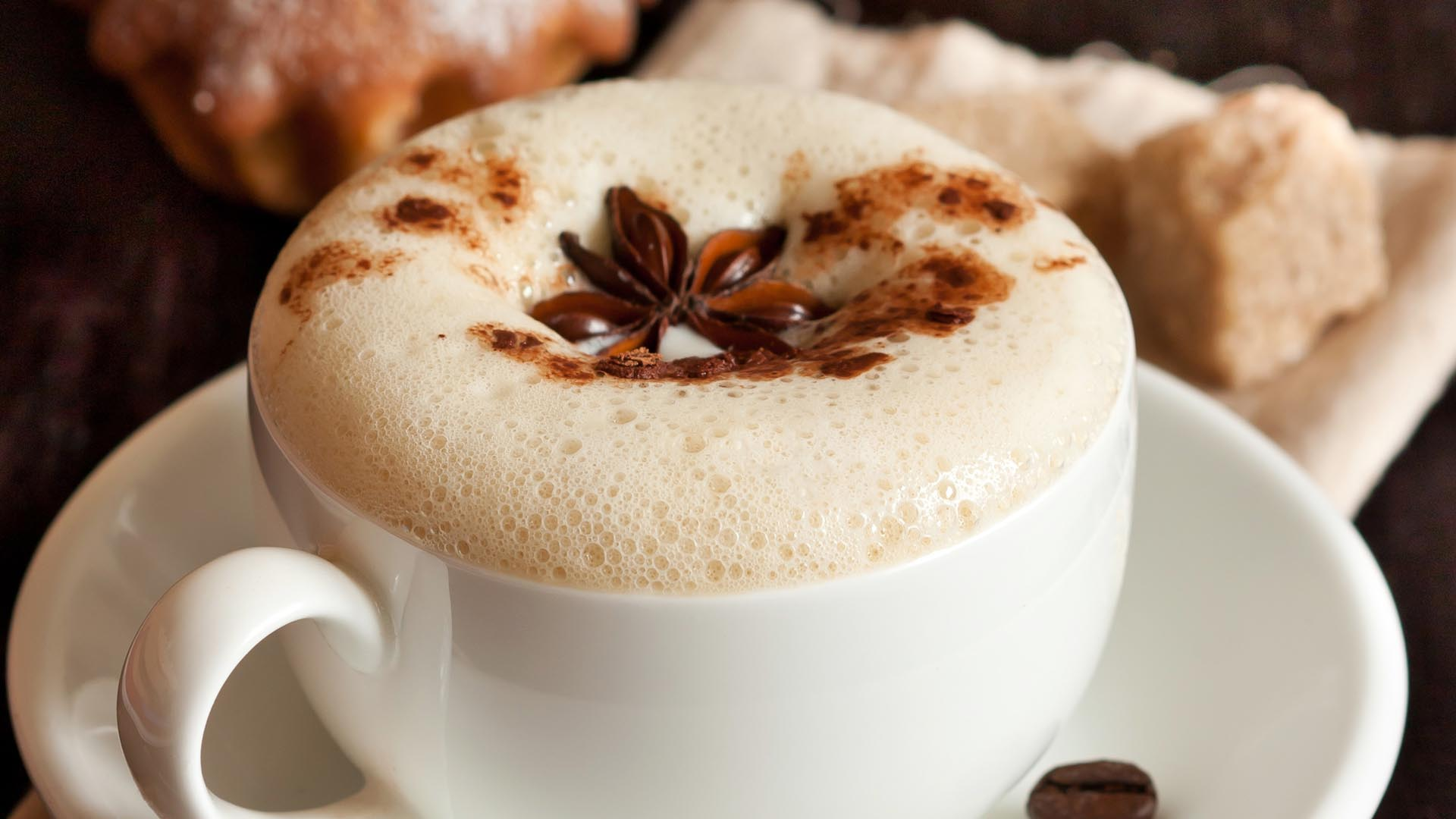 Filiżanka cappuccino z pianką i anyżem na tle cukru i wypieku.