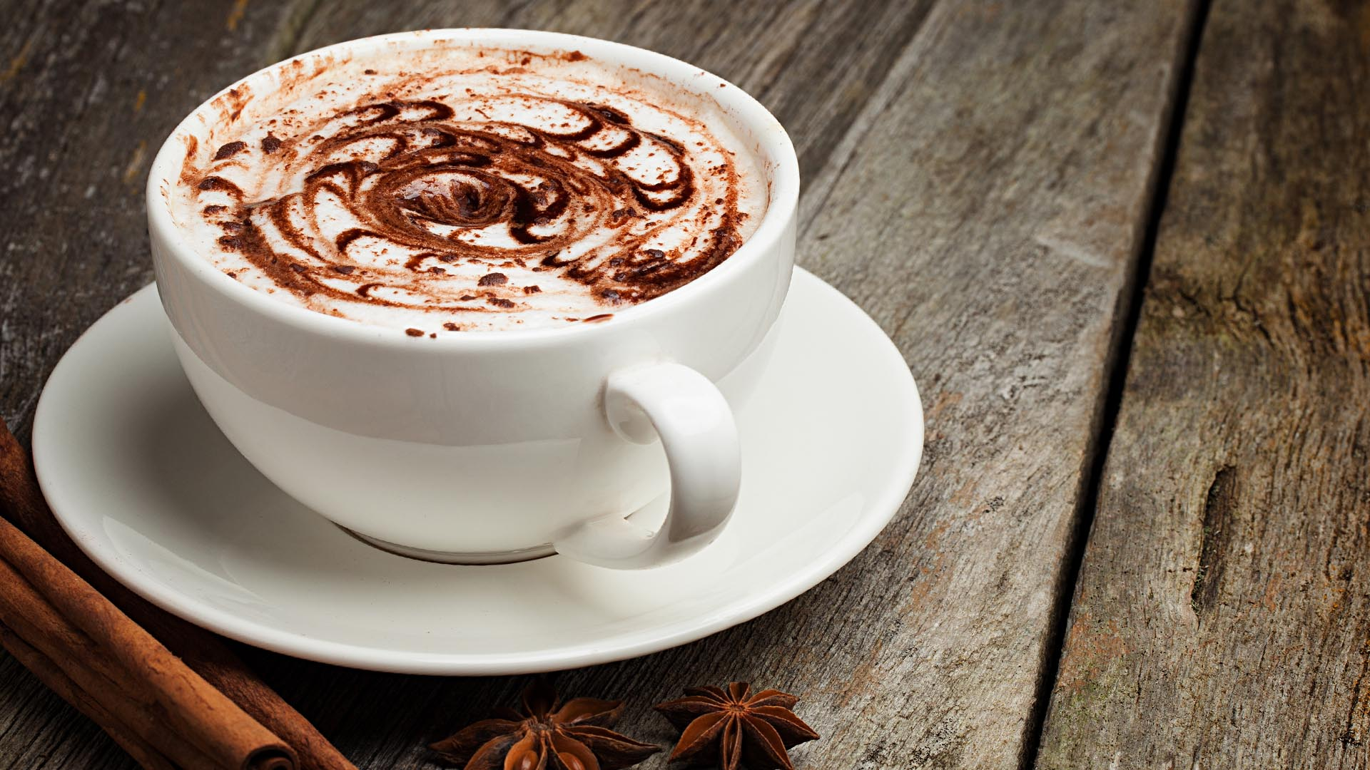 Biała filiżanka cappuccino z czekoladowym wzorem na drewnianym stole