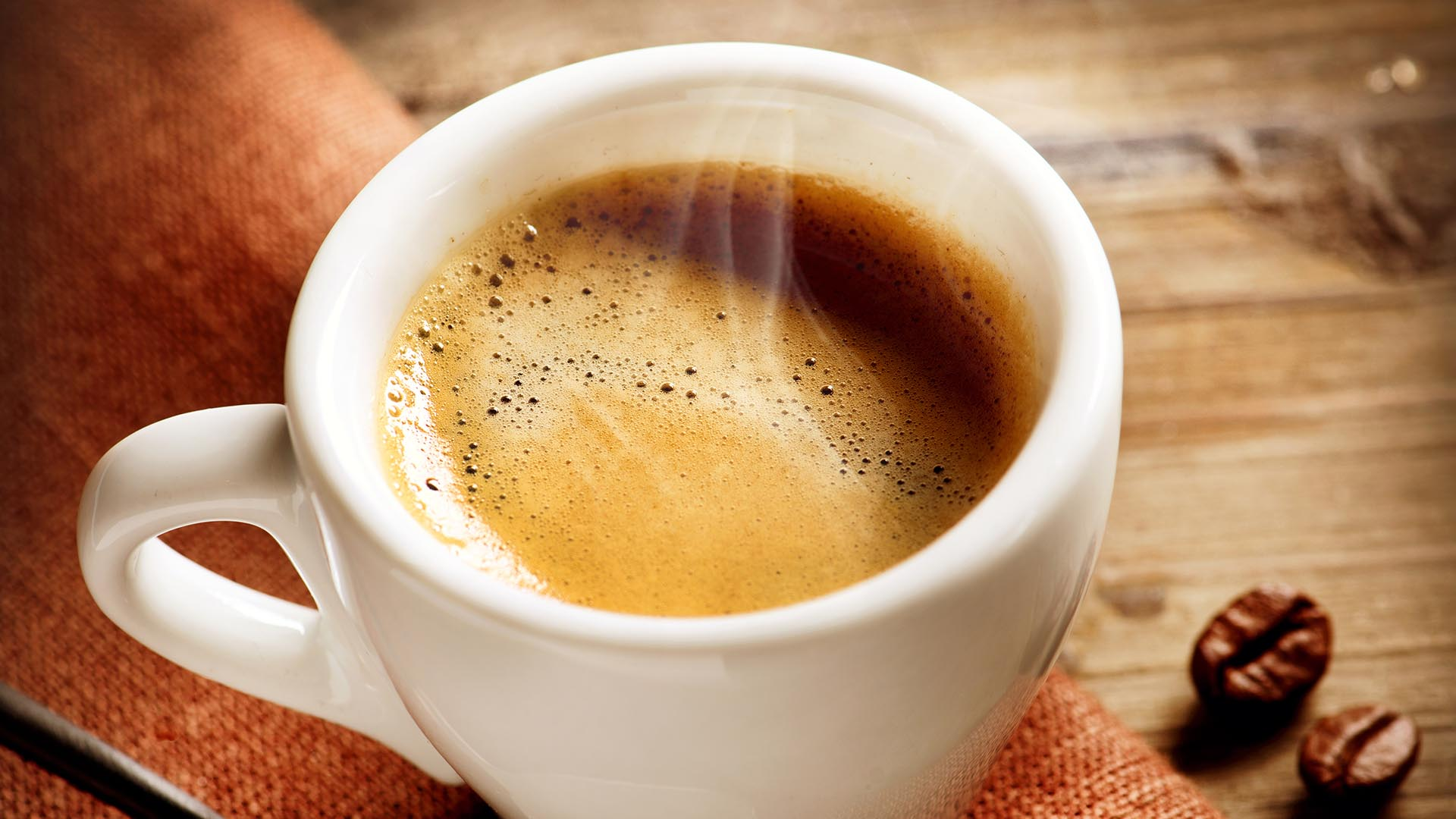 Biała filiżanka espresso na drewnianym stole z ziarnami kawy obok.