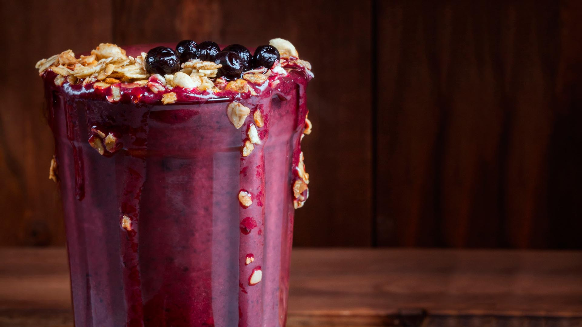 Smoothie jagodowe z granolą w wysokiej szklance na drewnianym tle.