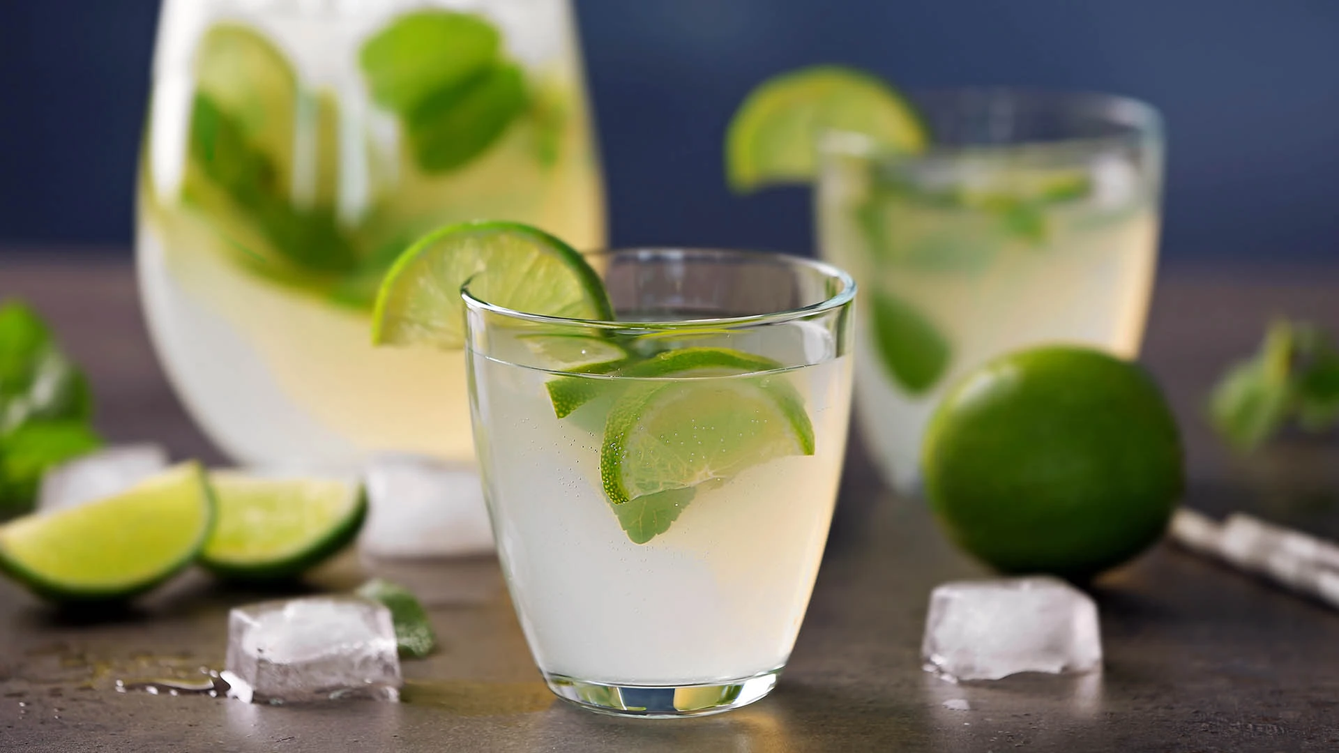 Szklanka lemoniady z limonką i lodem na stole, świeże limonki w tle.