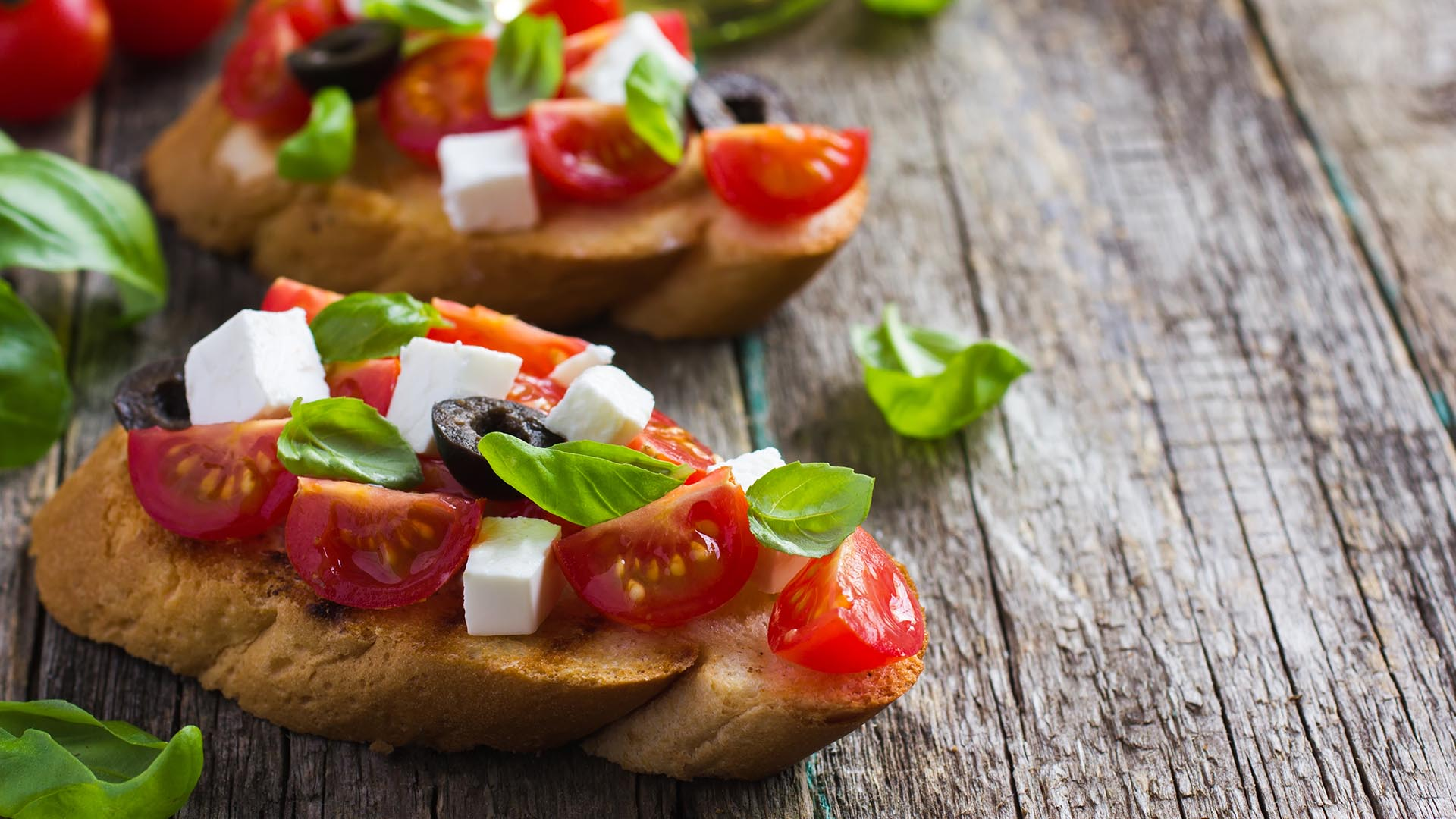 Bruschetta z pomidorami, bazylią i fetą na drewnianym stole.