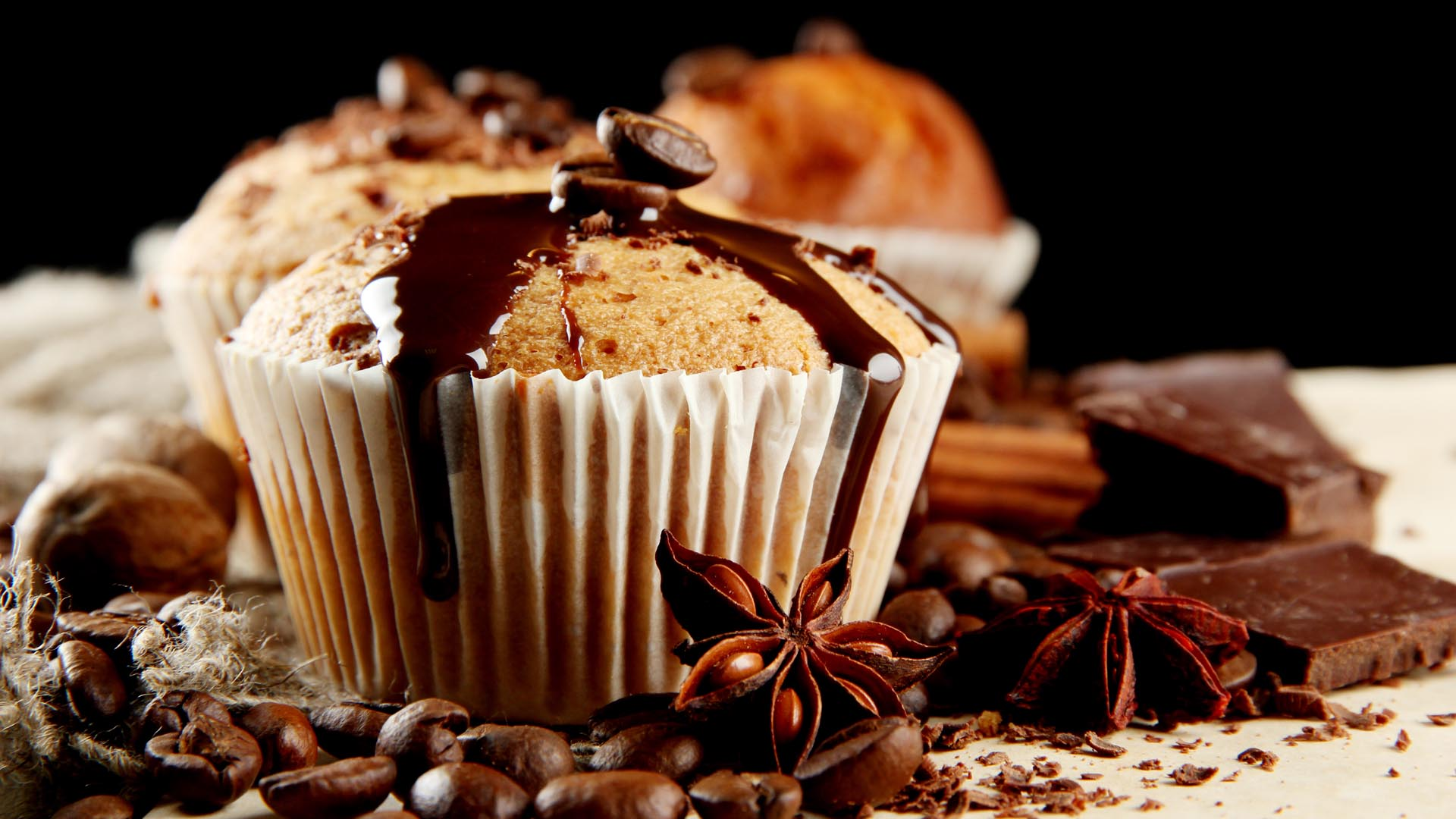 Muffinki z polewą czekoladową, otoczone ziarnami kawy i anyżem.