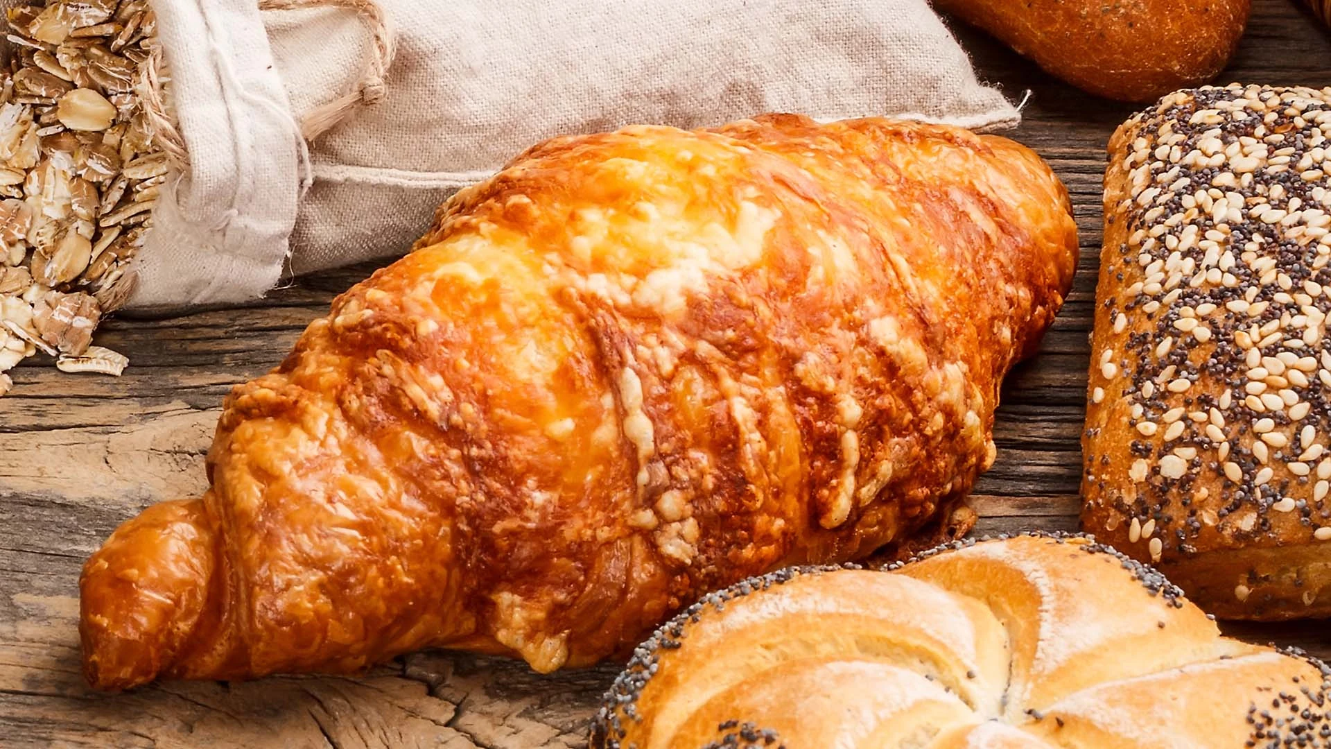 Świeże pieczywo na drewnianym stole, obok worek z płatkami owsianymi.