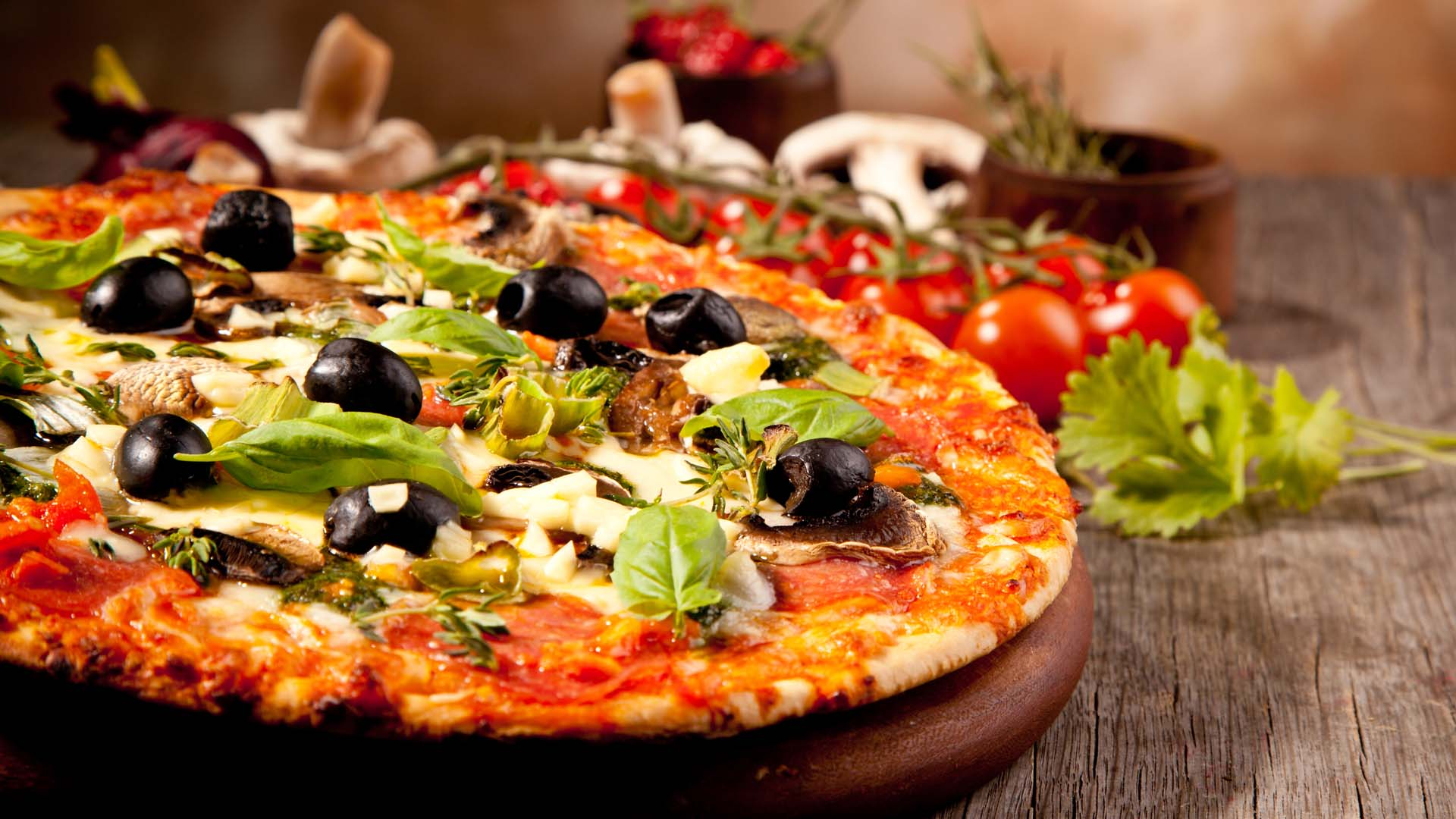 Włoska pizza z oliwkami, bazylią i pieczarkami na drewnianej desce