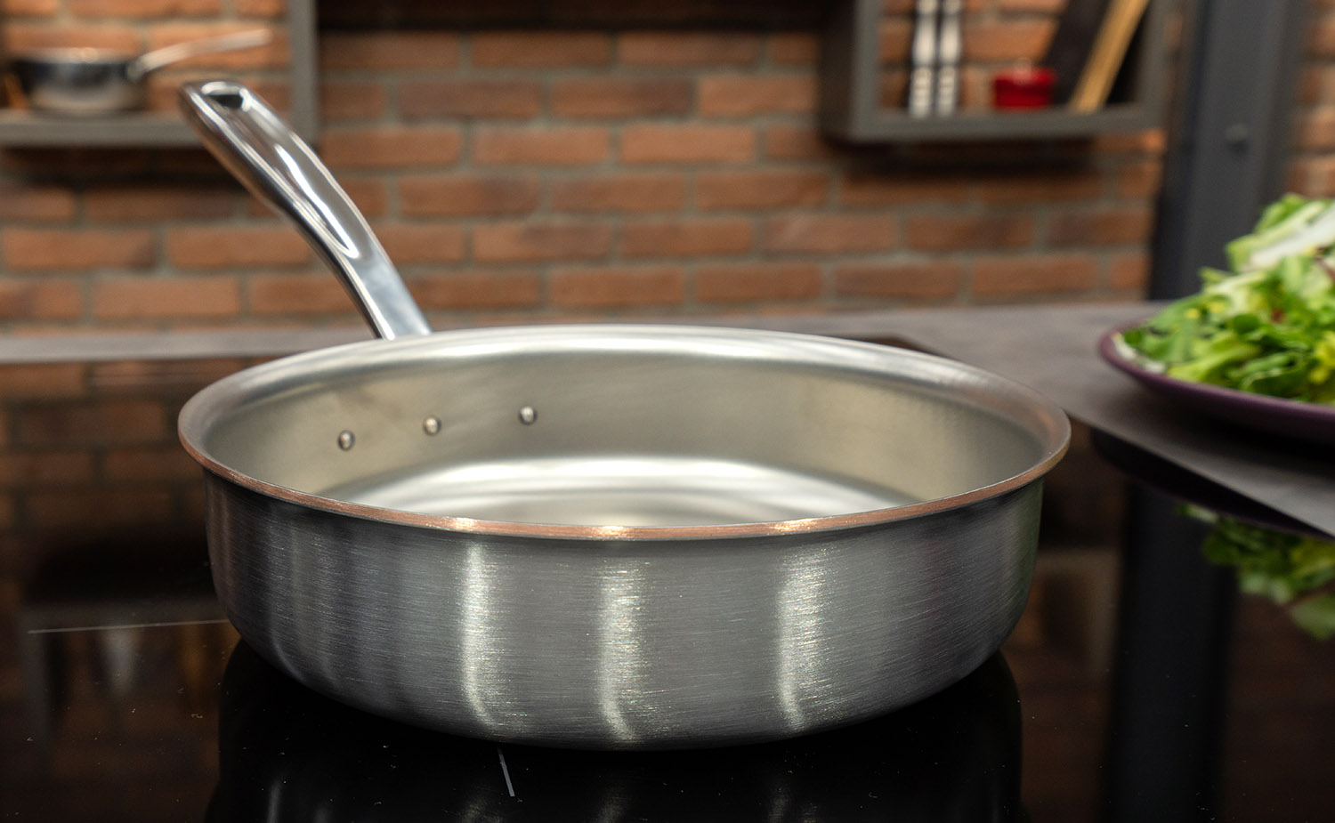 Ręcznie tworzona patelnia sauté Falk z pokrywką, stalowo-miedziana, Ø 24 cm, na tle kuchni.