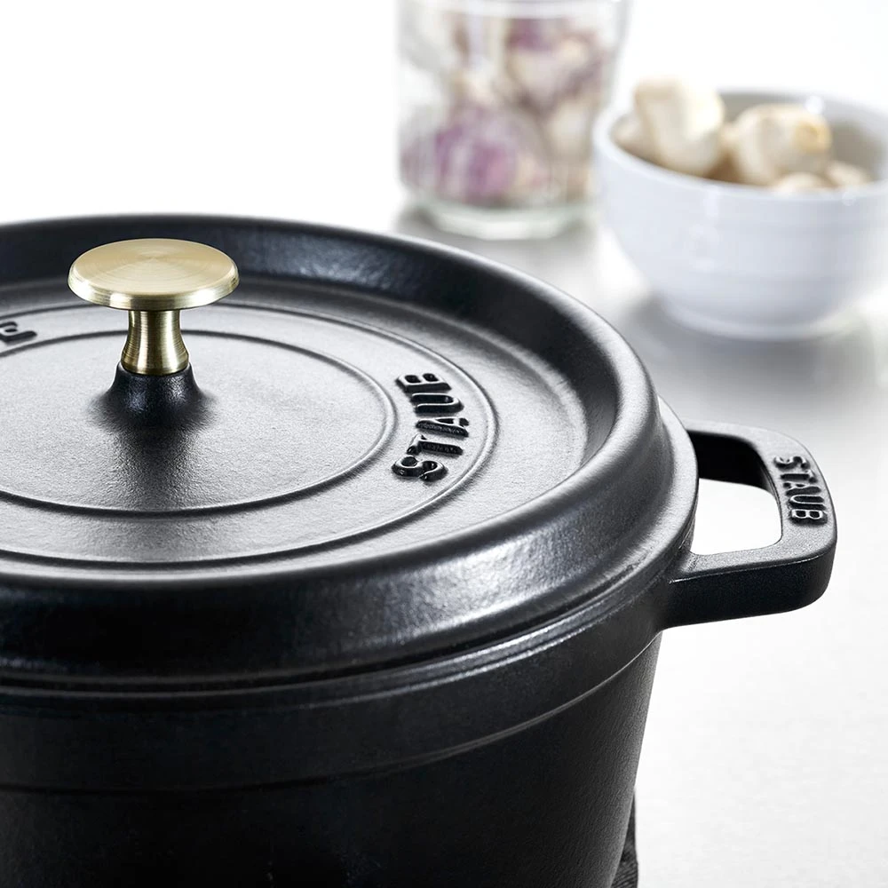 Czarny żeliwny garnek Staub z mosiężną gałką na pokrywce, idealny do gotowania.