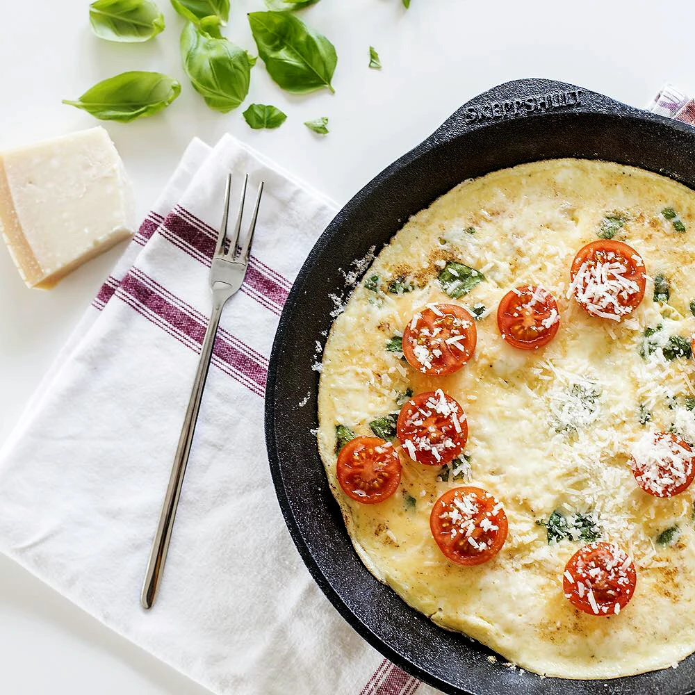 Żeliwna patelnia Skeppshult z omletem i świeżymi dodatkami Omlet z pomidorami i serem w żeliwnej patelni Skeppshult na kuchennym blacie
