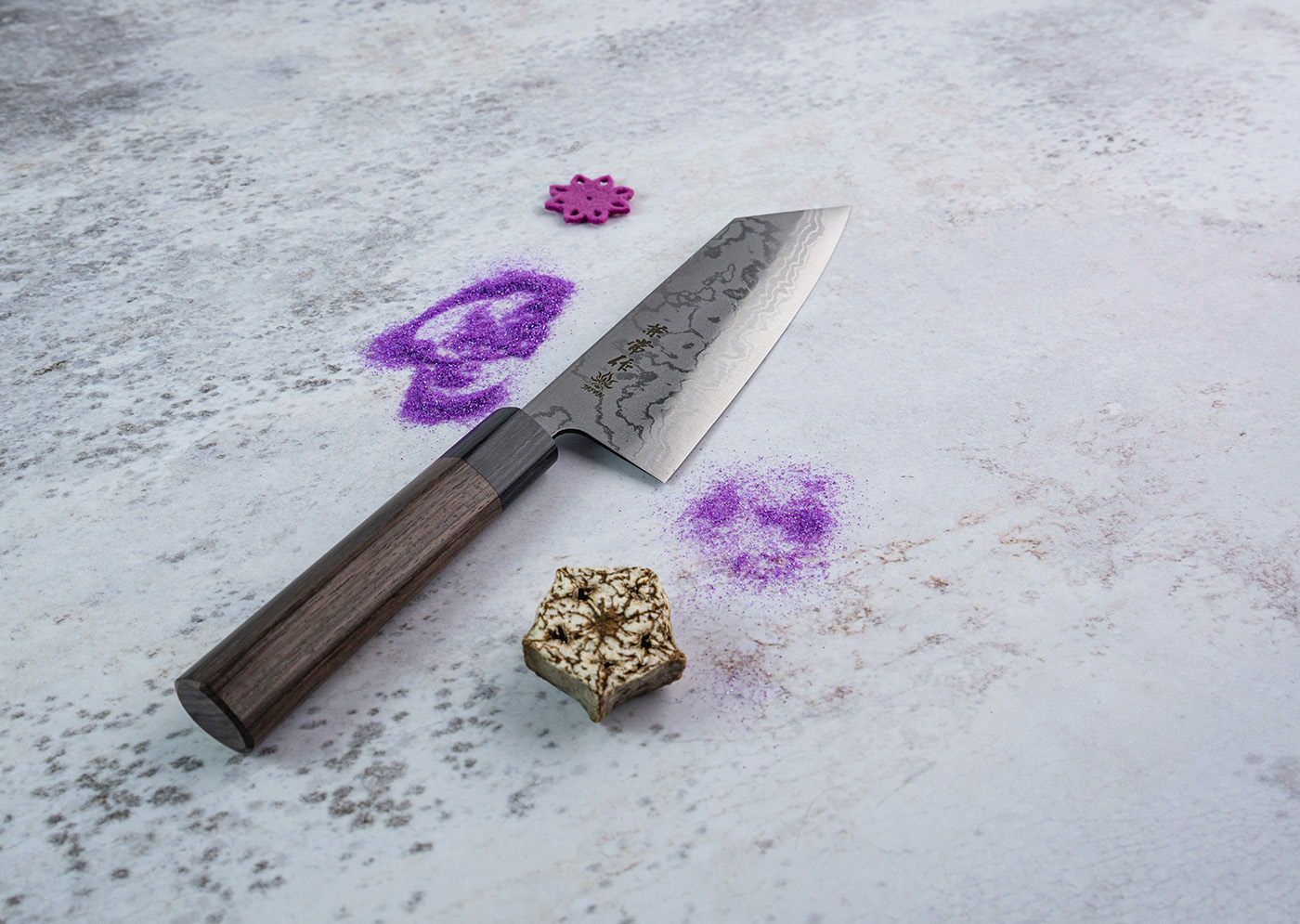Zen-Bokashi Bunka 17 cm z stali Aogami 2 na tle fioletowych ornamentów. Japoński nóż Bunka Kanetsune 17 cm na kamiennej powierzchni z fioletowym proszkiem i dekoracjami.