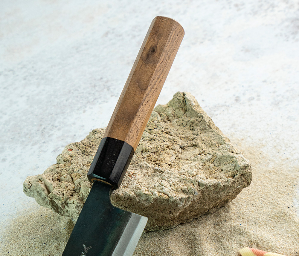 Tradycyjny nóż Santoku 17 cm z drewnianą rękojeścią, stal Aogami 2. Japoński nóż Santoku 17 cm z drewnianą rękojeścią na tle kamienia i piasku.