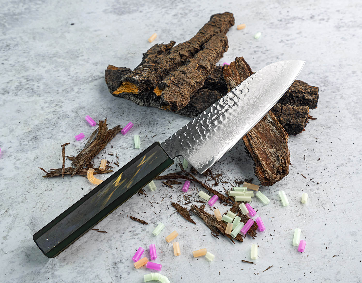 Japoński nóż Santoku 17 cm na tle kory i kolorowych drobinek.