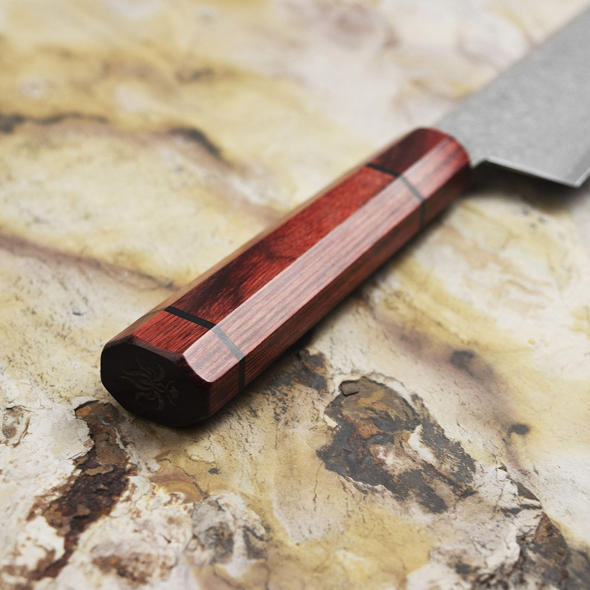 Drewniana rękojeść noża Kanetsune na tle kamiennego blatu. Rękojeść noża Santoku Minamo-Kaze z drewna na marmurowym tle.