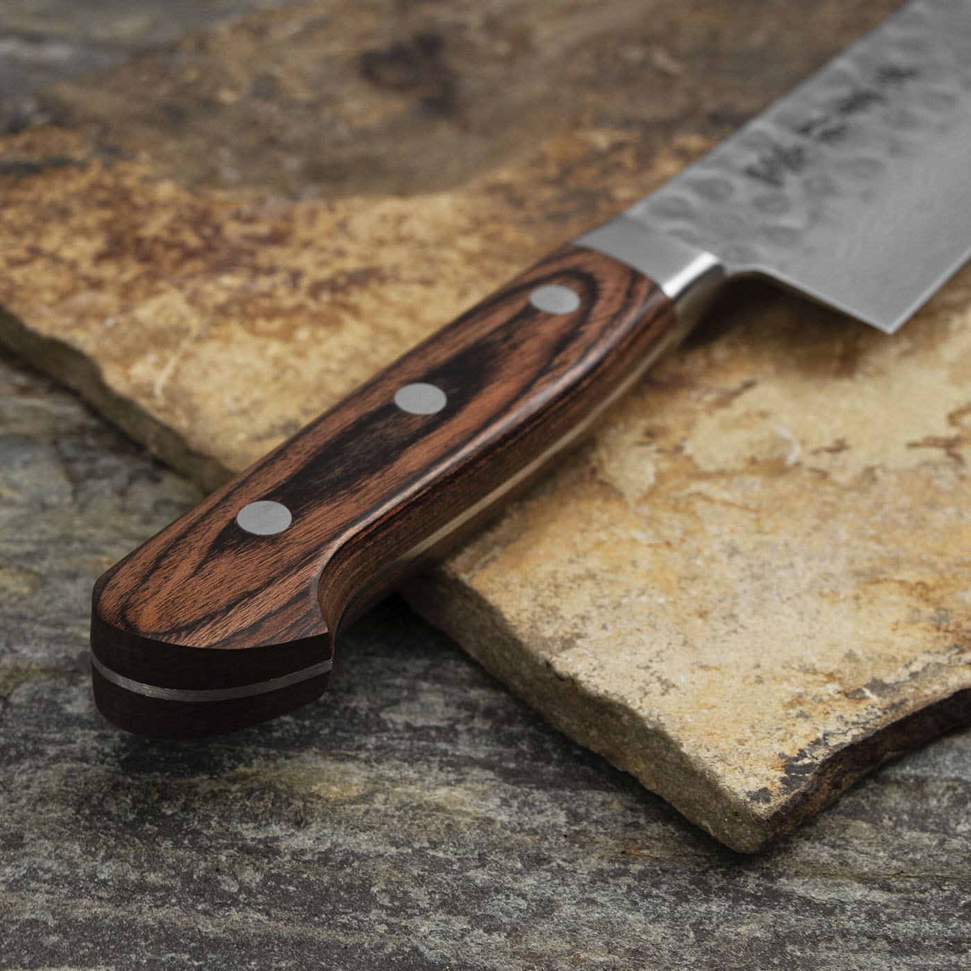 16-warstwowy nóż Santoku z VG-10 na tle kamienia. Japoński nóż Santoku 18 cm z drewnianą rękojeścią na kamiennej powierzchni.