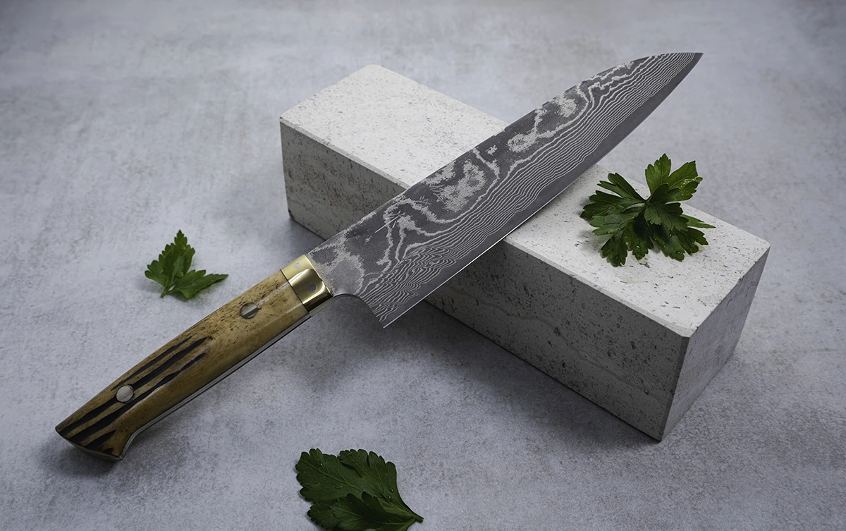 Japoński nóż Santoku na tle kamiennego bloku, ozdobiony liśćmi pietruszki.