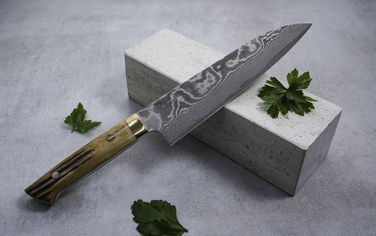 Japoński nóż Santoku na tle kamiennego bloku, ozdobiony liśćmi pietruszki.