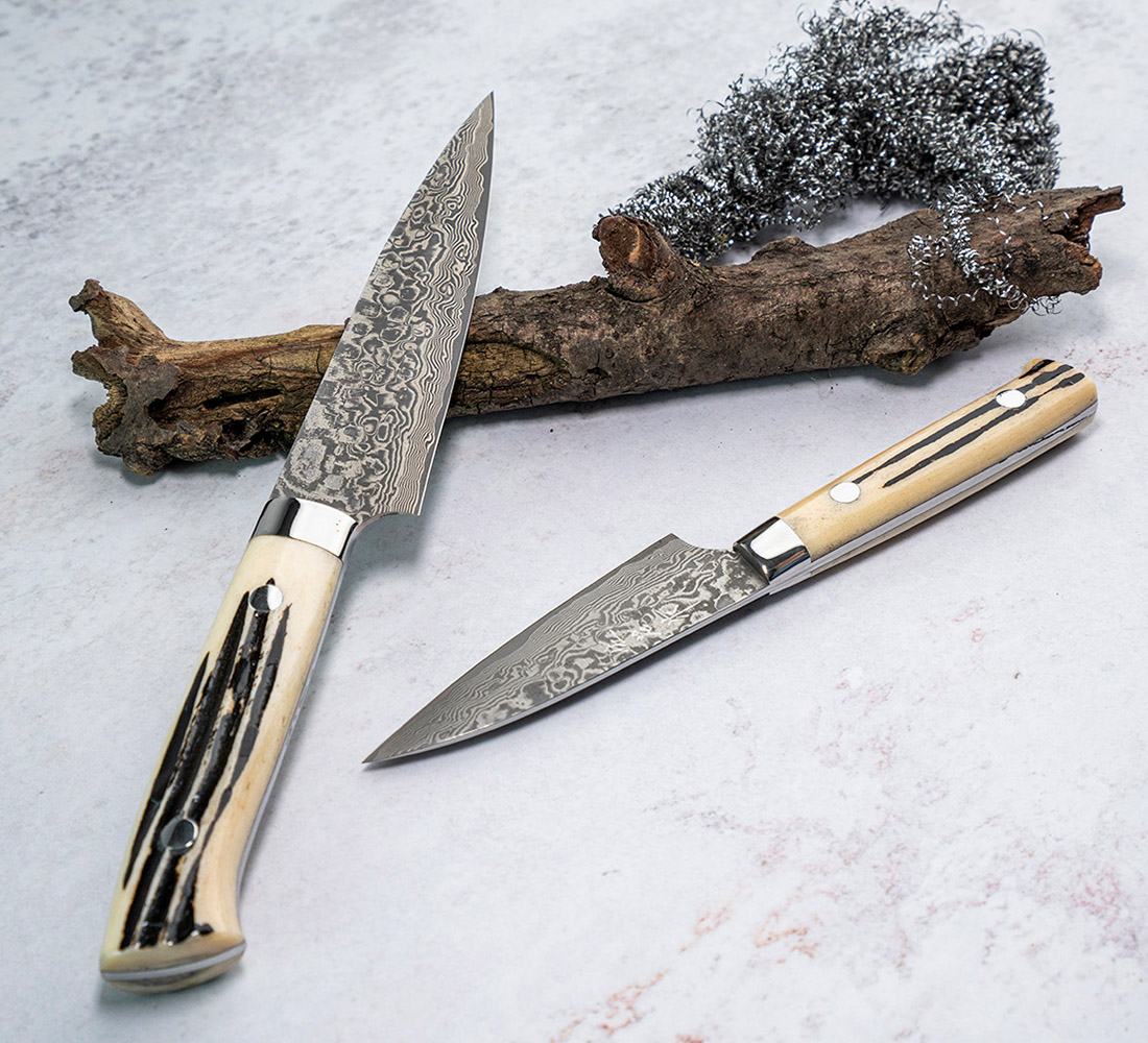 Nóż Shotoh 13 cm, damasceńska stal R2, Takeshi Saji, obok drewna i metalowej spirali. Uniwersalny nóż Shotoh 13 cm z damasceńskiej stali, Takeshi Saji, na tle drewna i stali.