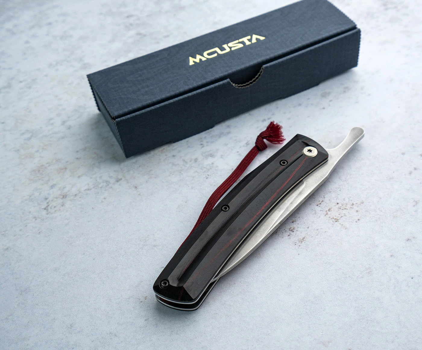 Japoński składany nóż Friction Folder z ostrzem VG-10, leżący obok pudełka Mcusta.