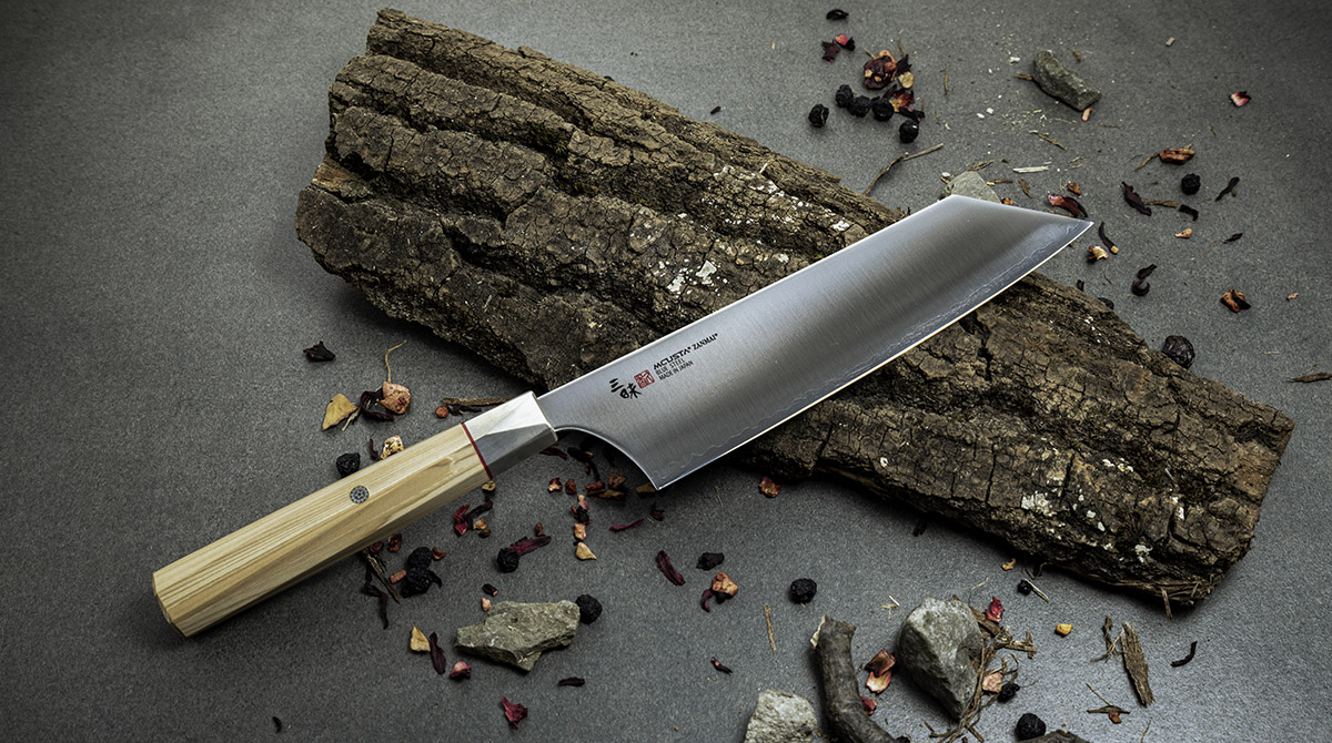 Japoński nóż Bunka, stal Aogami Super, 18 cm, na tle kory i suszonych ziół.