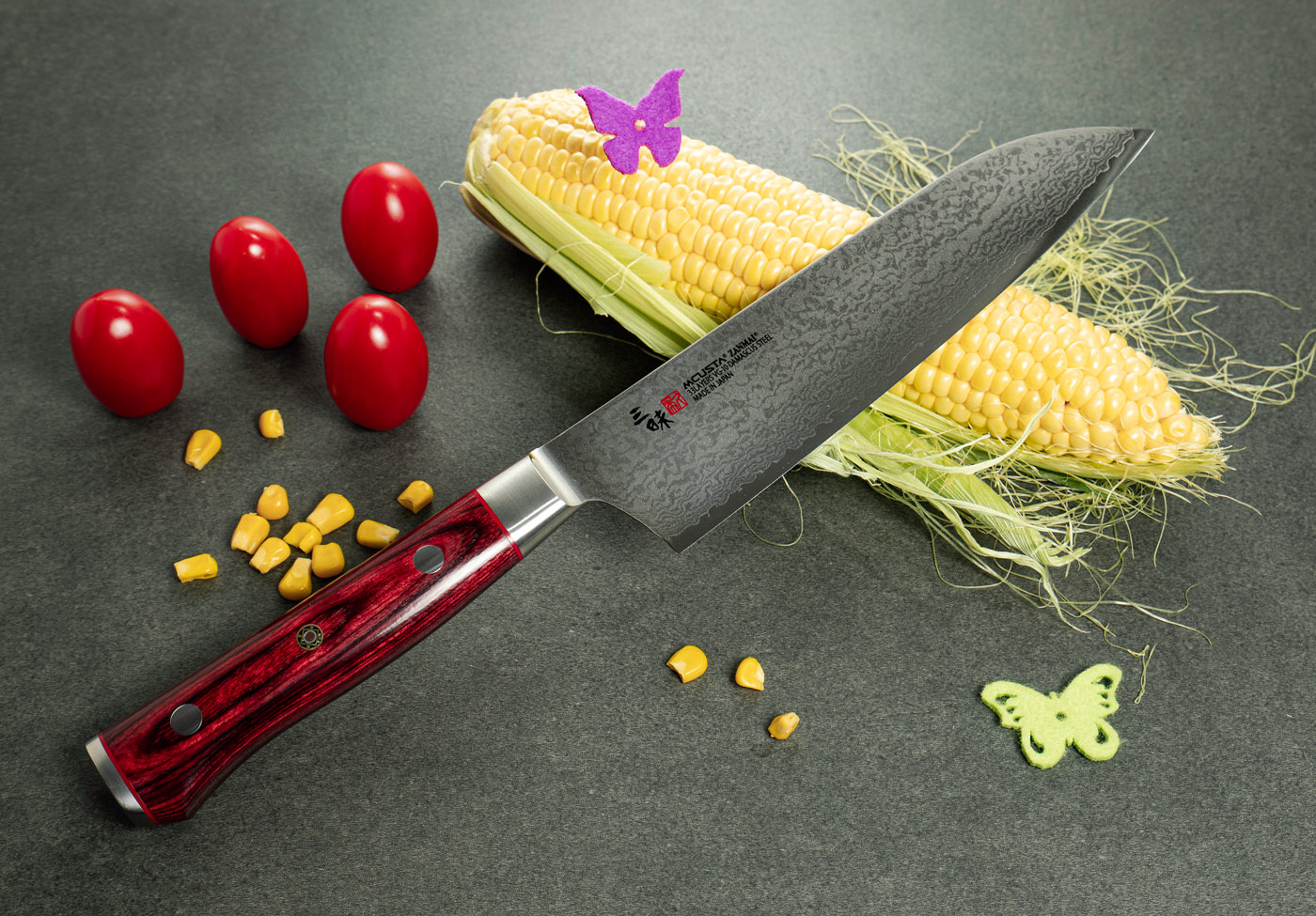 33-warstwowy nóż Santoku Mcusta Zanmai z kukurydzą i pomidorami Japoński nóż Santoku Mcusta Zanmai na tle kukurydzy i pomidorów