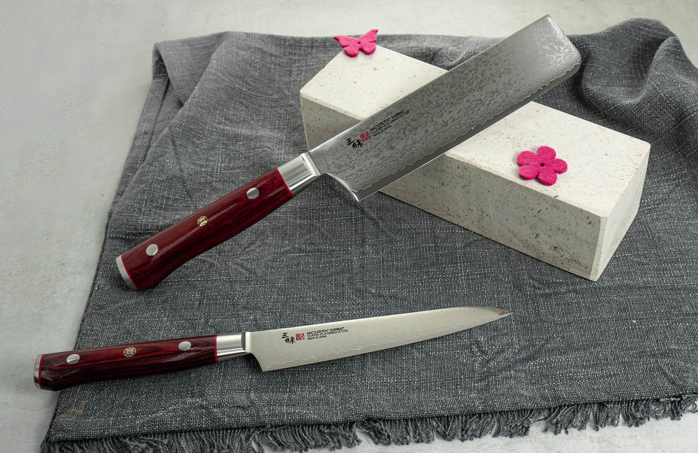 Elegancki nóż Gyutoh Mcusta Zanmai 24 cm z japońskiej stali. Japoński nóż kuchenny Gyutoh Mcusta Zanmai na tle szarej tkaniny.