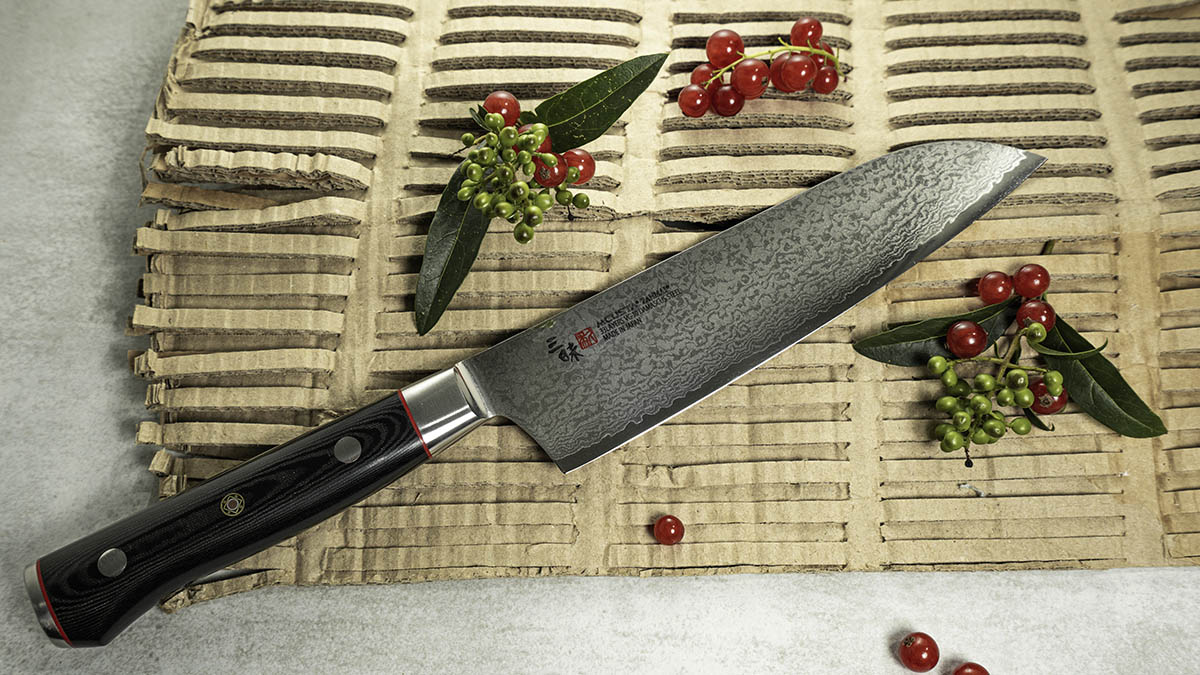 33-warstwowy nóż kuchenny Santoku Mcusta Zanmai z dekoracją Japoński nóż Santoku Mcusta Zanmai na tle ozdobnym z liśćmi i jagodami