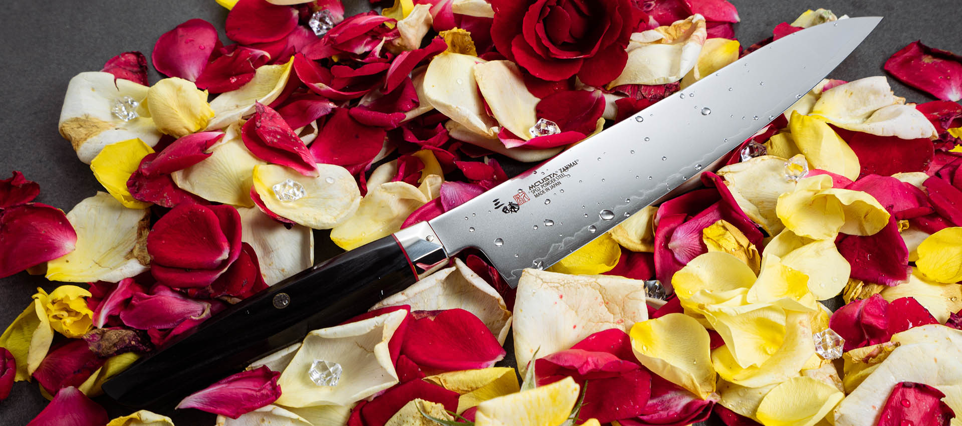 Nóż Santoku Mcusta Zanmai na tle płatków róż i kryształków