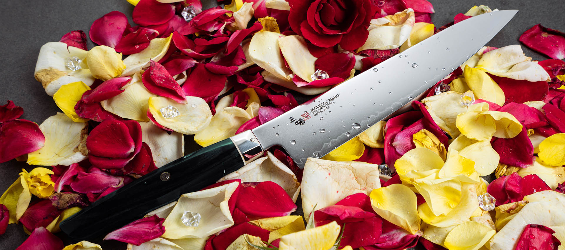 Japoński nóż Ko-Santoku Mcusta Zanmai na płatkach róż w kolorach czerwonym, żółtym i białym.