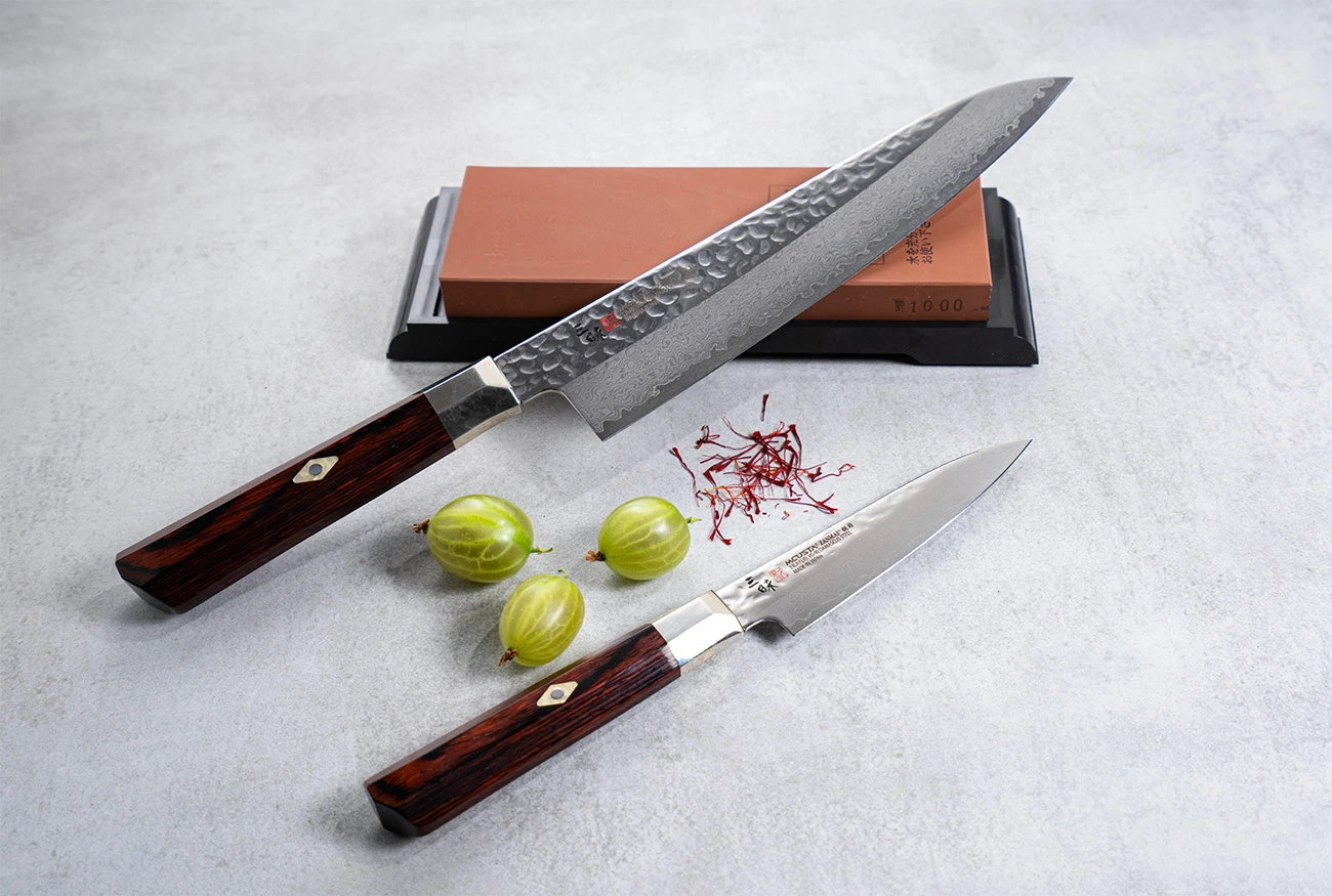 Młotkowany nóż Santoku Mcusta Zanmai z damasceńskiej stali na tle kamienia do ostrzenia.