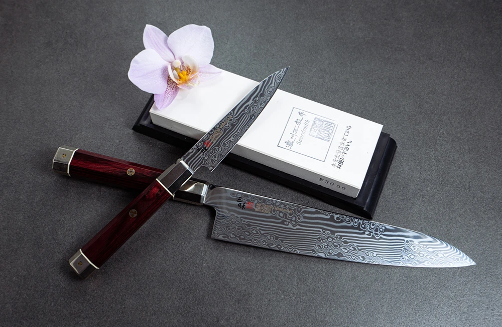 Nóż Nakiri 32-warstwowy z plecionej stali, Mcusta Zanmai, obok elegancka orchidea.