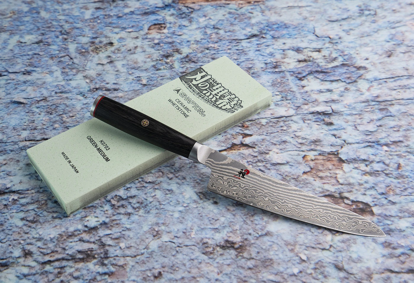 Damasceński nóż Nakiri 17 cm Miyabi na tle kamienia ceramicznego. Japoński nóż Nakiri 17 cm z damasceńskiej stali, leżący na kamieniu ceramicznym.