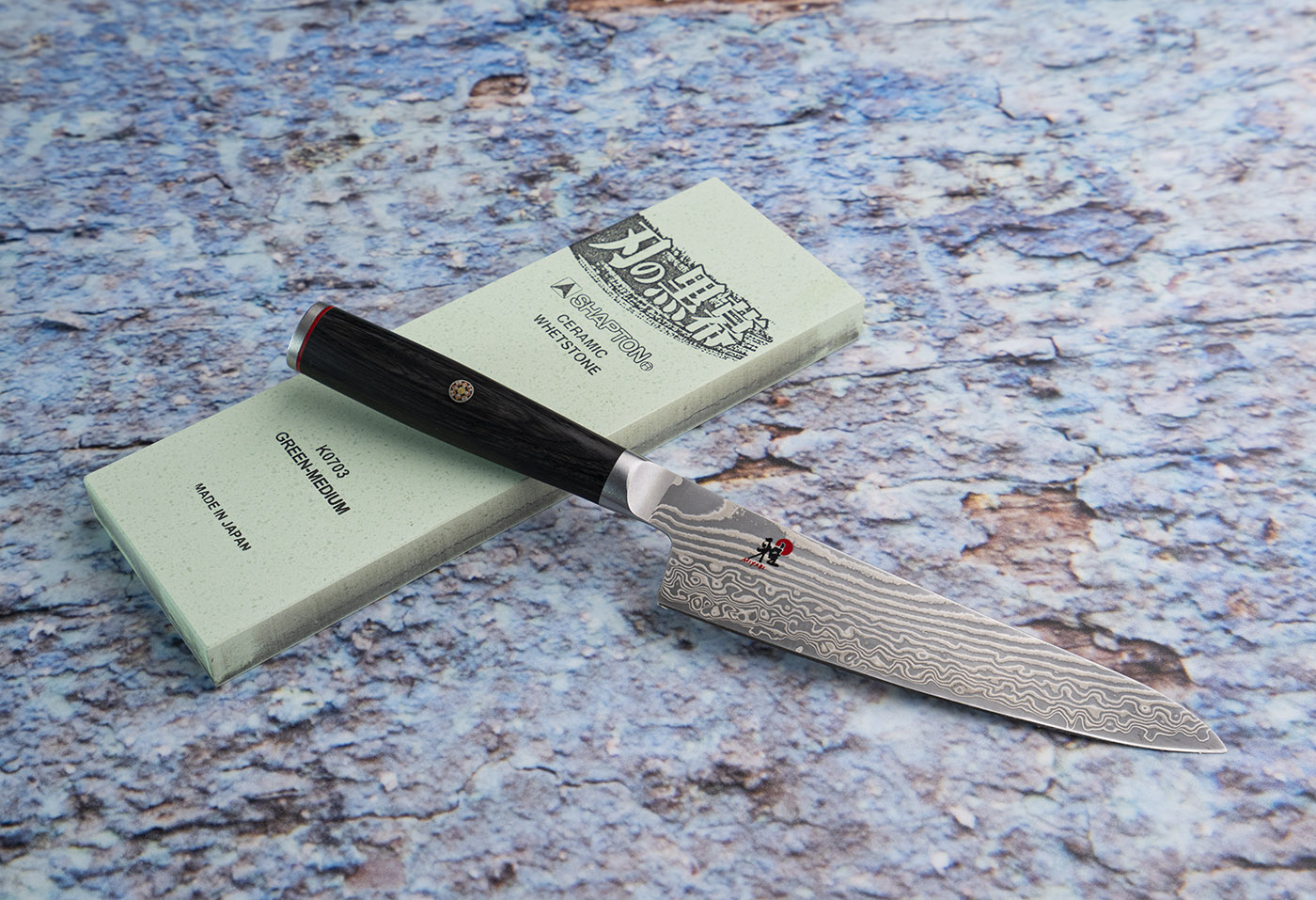 Damasceński nóż Nakiri 17 cm Miyabi na tle kamienia ceramicznego. Japoński nóż Nakiri 17 cm z damasceńskiej stali, leżący na kamieniu ceramicznym.