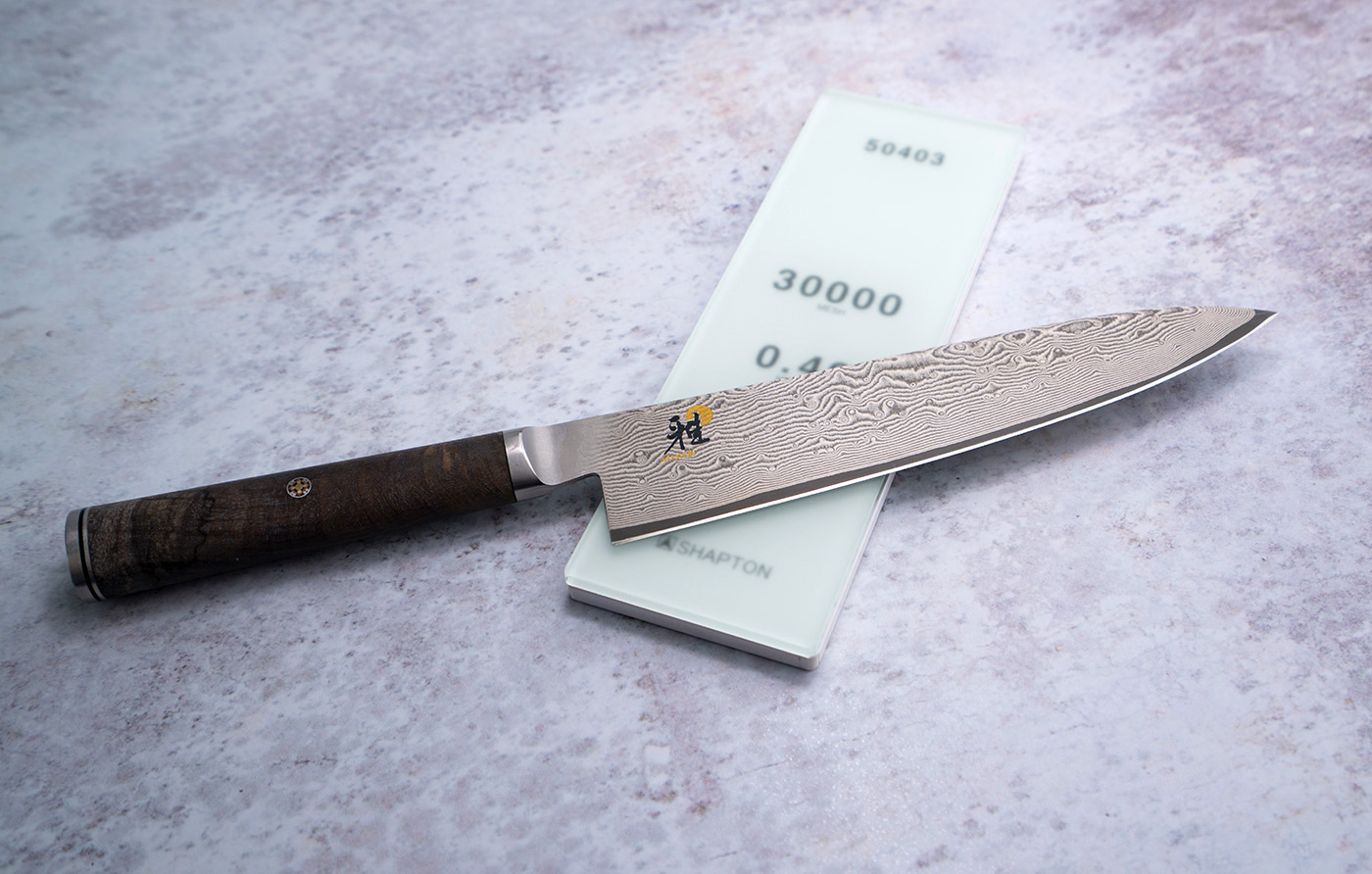 Damasceński nóż Santoku Miyabi na tle kamienia do ostrzenia