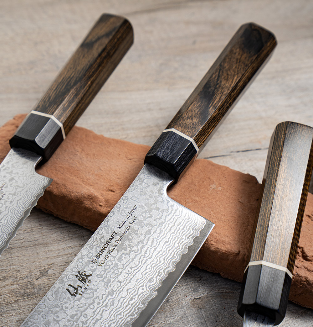 Czerniony nóż Bunka Suncraft o długości 16,5 cm z damasceńską stalą. Japoński nóż Bunka, 33-warstwowy, z drewnianą rękojeścią na tle cegły.