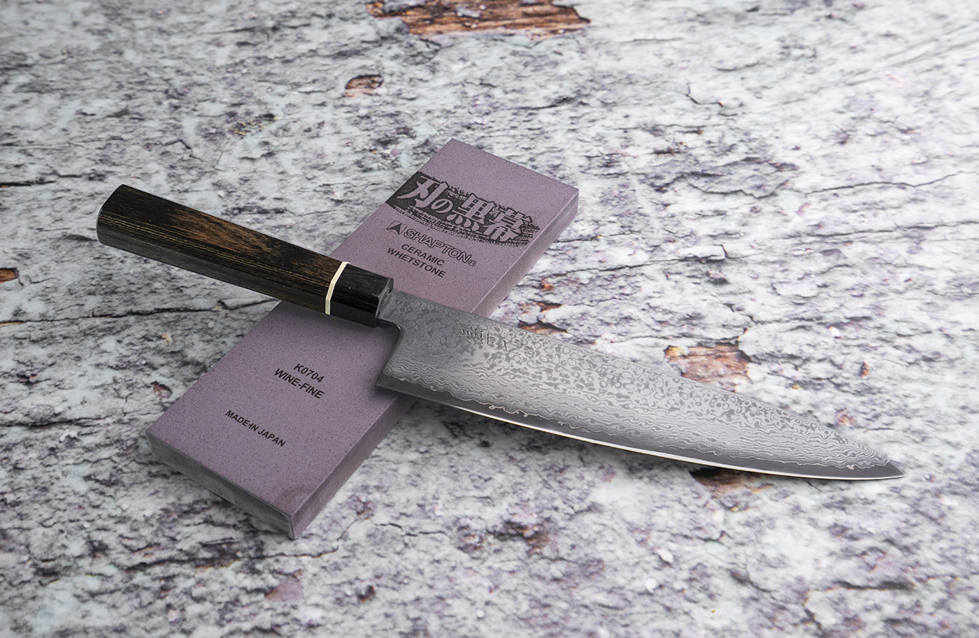 Elegancki japoński nóż Bunka 20 cm z 33-warstwowej stali na tle kamienia do ostrzenia.