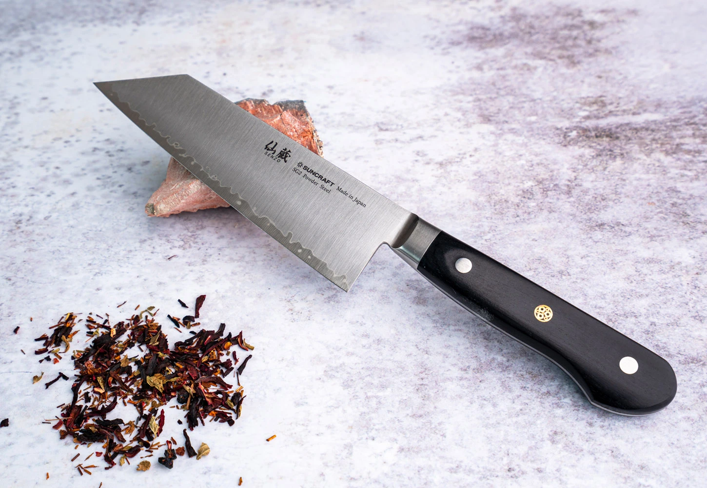Japoński nóż Bunka Suncraft, stal SG2, 16,5 cm, na tle przypraw i kamienia.