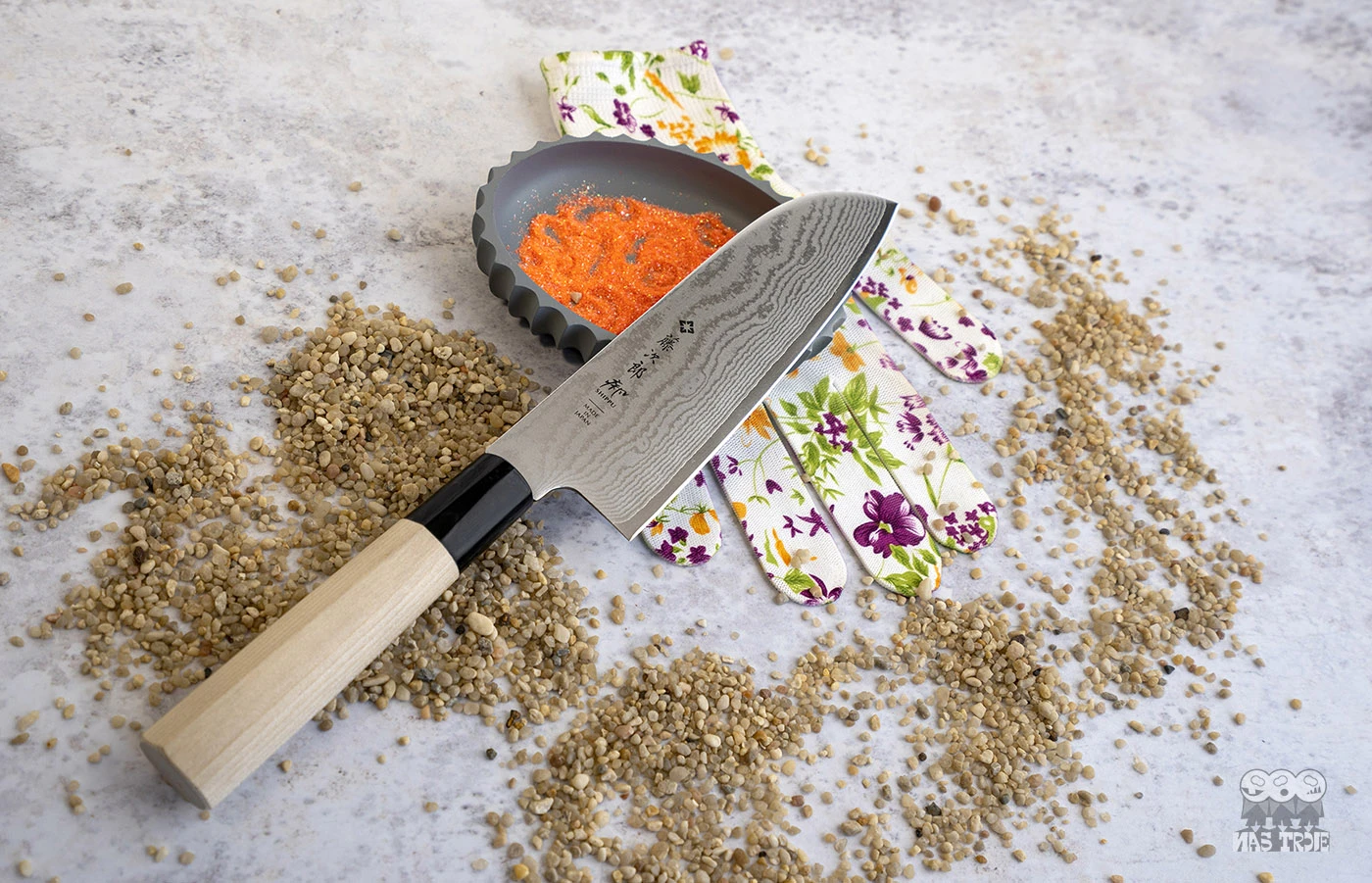 Japoński nóż Santoku Tojiro na tle kolorowych rękawic kuchennych i przypraw.