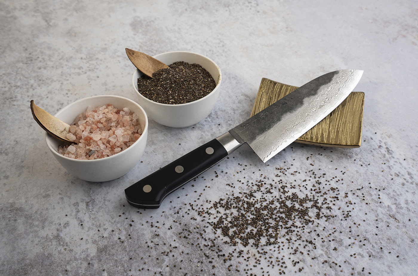 Nóż Santoku 17 cm z damasceńskiej stali, w towarzystwie przypraw, na eleganckim tle. Japoński nóż Santoku z 63-warstwowej stali, obok miseczki z solą i ziarnami, na marmurowym tle.
