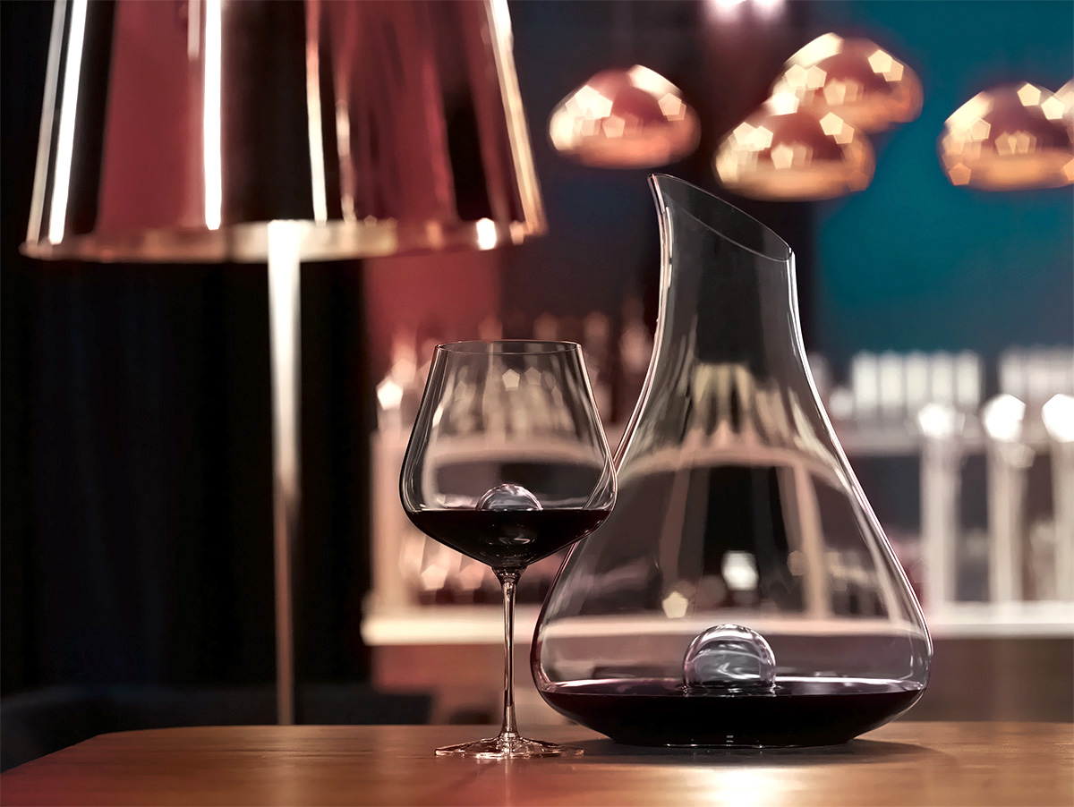 Ręcznie dmuchana karafka-dekanter i kieliszek z czerwonym winem na tle eleganckiego wnętrza.