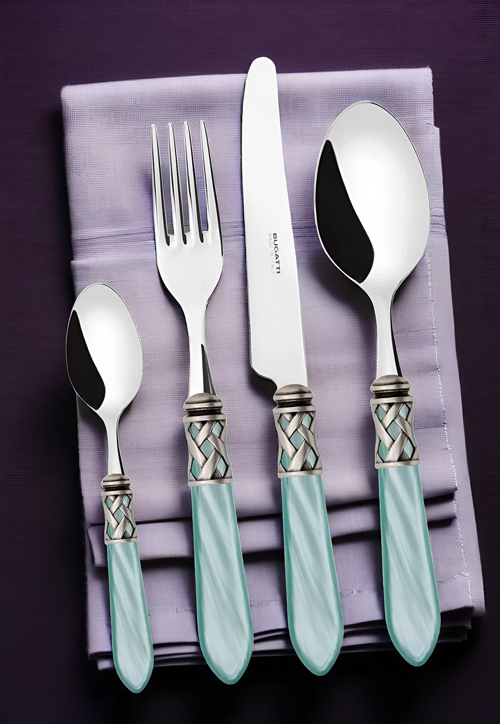 Eleganckie sztućce Aladdin Aqua Green na fioletowej serwetce. Sztućce Aladdin Aqua Green z wykończeniem w stylu starego srebra na serwetce.