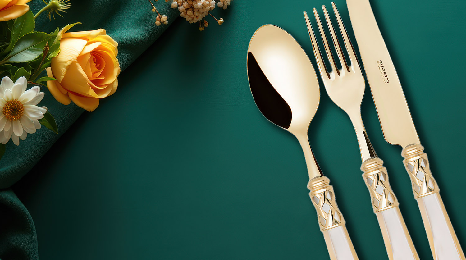 Zestaw sztućców Aladdin Gold Ivory na tle zielonej tkaniny i kwiatów